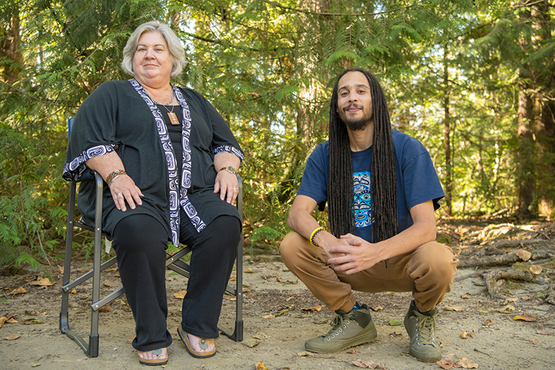 A mother and son out in nature, with the mother sitting in a chair and her son next to her