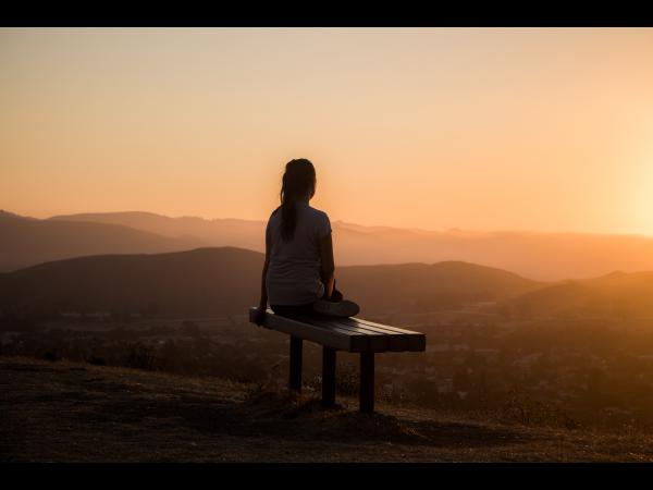 Woman sitting on bench at sunset